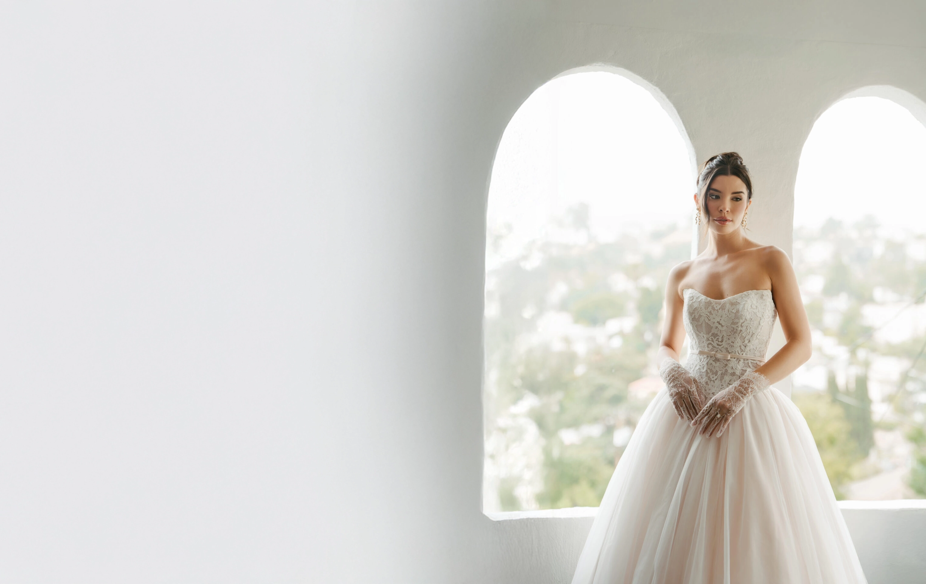 A joyful bride in lace laughing with roses, peonies, and eucalyptus against a soft peach backdrop — Becker's Bridal